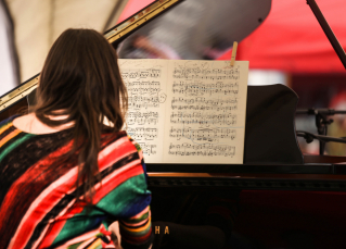 een vrouw speelt muziek op een vleugelpiano en kijkt daarbij naar een partituur