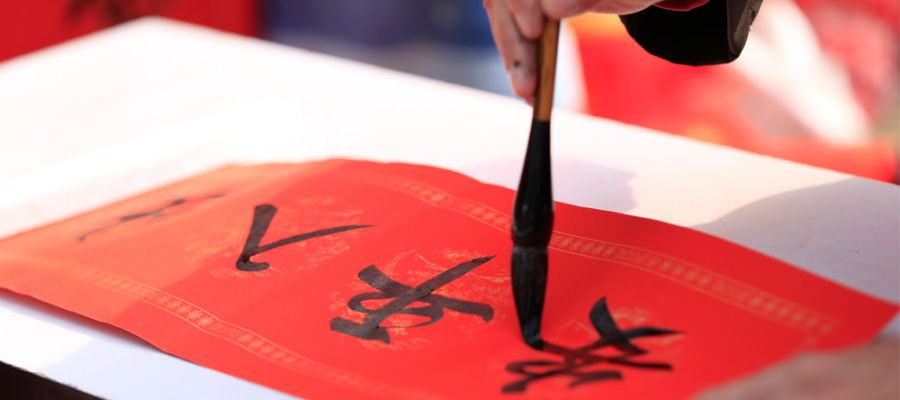 een hand tekent met penseel en inkt een chinees teken op een rood papier