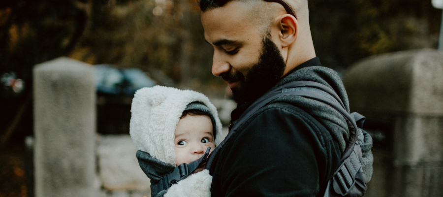 man met baard kijkt naar baby die hij met een draagzak op zijn buik draagt