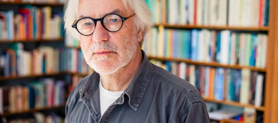 Portretfoto van de schrijver Erik Vlaminck, die voor een gevulde boekenkast staat. Erik draagt een bril en een jeanshemd.