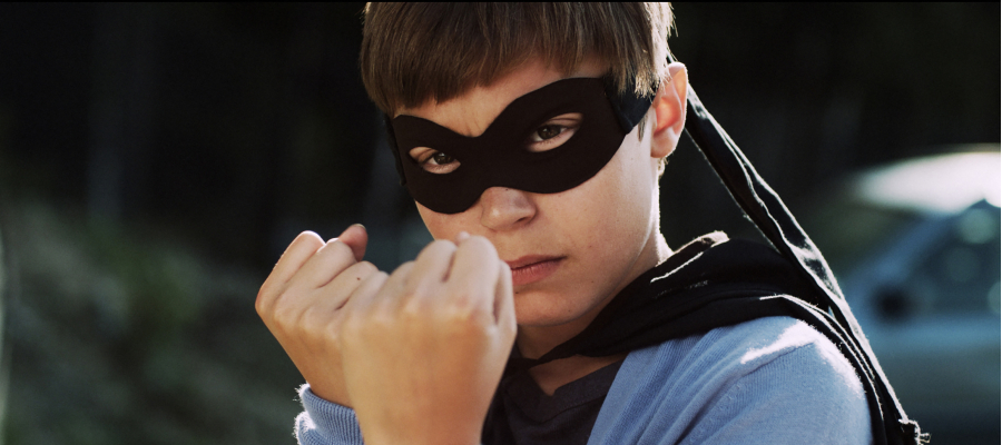 jongen met een zwart masker voor zijn ogen en een zwarte cape houdt de vuisten gebald voor zijn gezicht