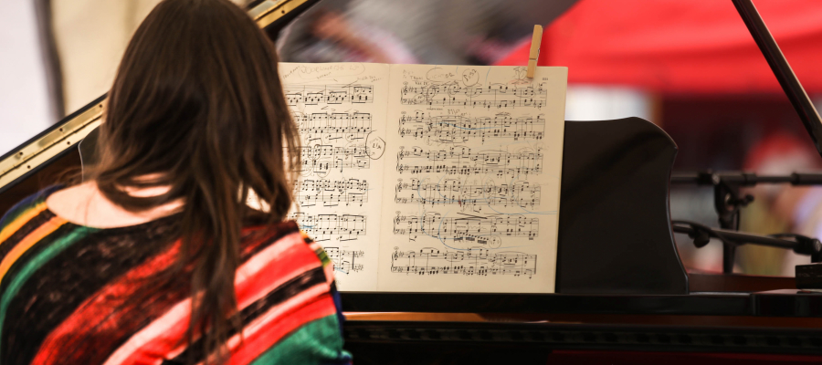 vrouw speelt op een vleugelpiano en kijkt op een pianopartituur met veel notities