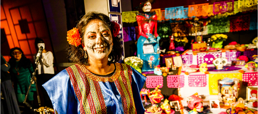 vrouw met beschilderd gezicht en papieren bloem in het haar poseert aan het altaar voor de Dag van de Doden