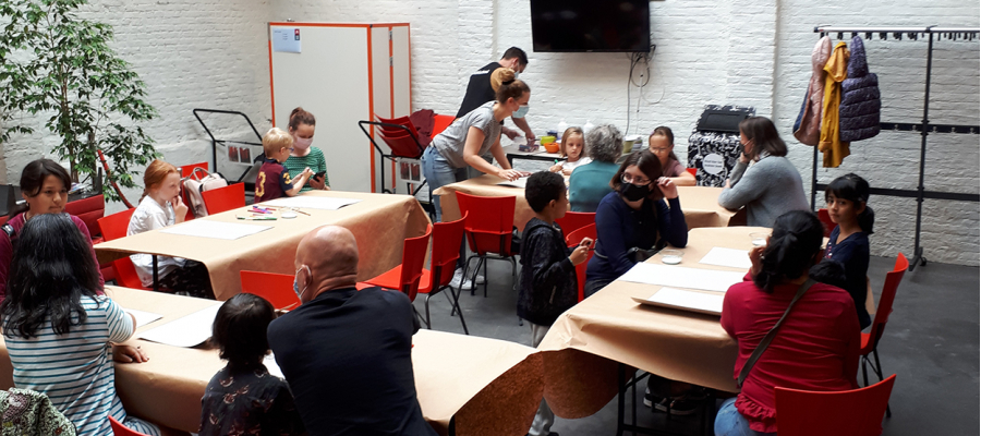 kinderen en (groot)ouders zitten aan tafels voor een knutselworkshop in de jeugdzone van bib Permeke