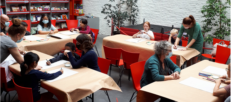 kinderen en (groot)ouders zitten aan tafels voor een knutselworkshop in de jeugdzone van bib Permeke
