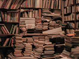 man zit tussen stapels boeken en boekenkasten